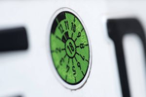 Die grüne TÜV-Plakette auf einem Nummernschild mit Tiefenschärfe fotografiert.