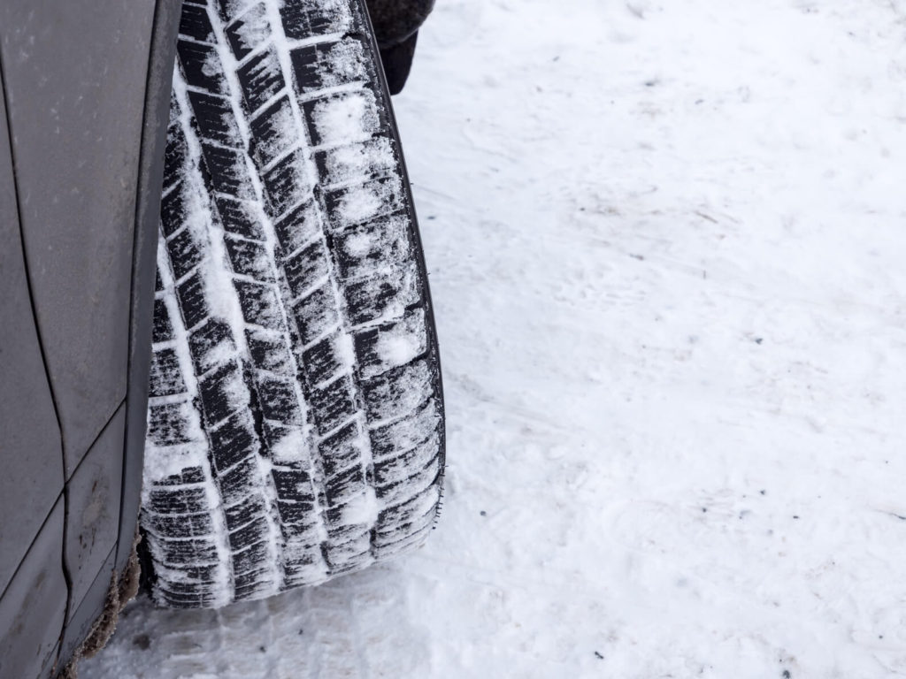 Winterreifens eines Pkw auf schneebedeckter Fahrbahn mit Schnee im Reifenprofil.