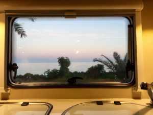 Aussicht auf einen Sonnenuntergang am Meer aus einem Wohnmobilfenster.